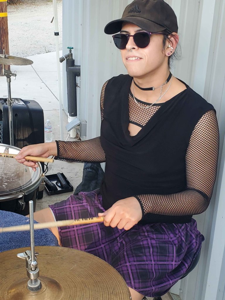 Vivi Dusk drumming outside in purple skirt.